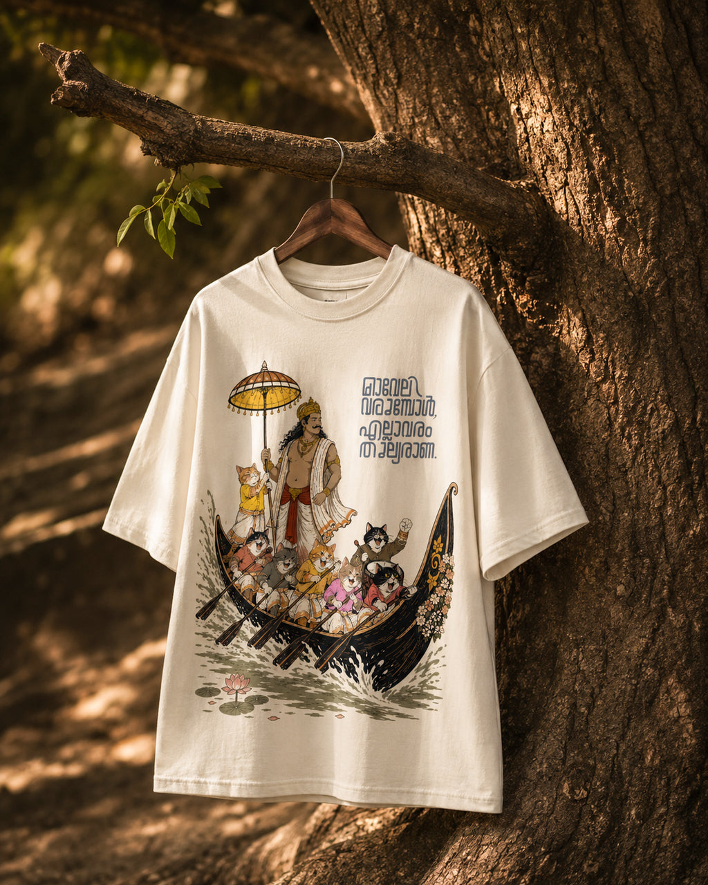 Off-white Mild Popie All Are Equal oversized graphic T-shirt featuring Mahabali, Kerala's iconic snake boat race, cats, Indian dogs, and Malayalam typography, displayed hanging on a tree branch.