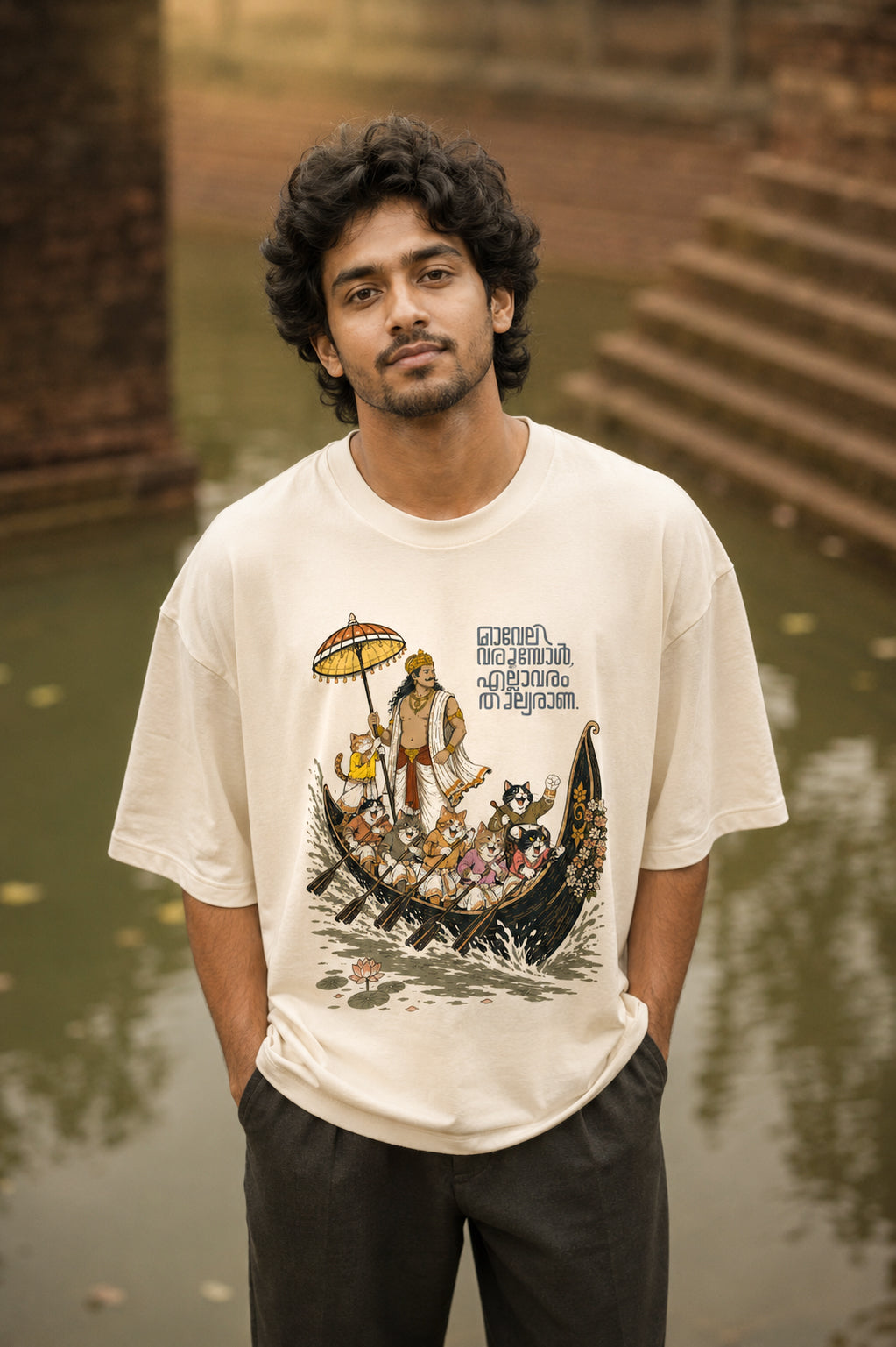 Model wearing Mild Popie's All Are Equal oversized graphic T-shirt featuring Mahabali, Kerala snake boat race, cats, and Indian dogs celebrating Onam.