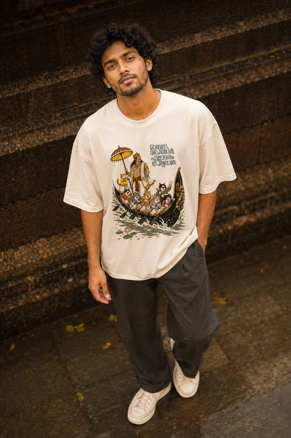 Man wearing Mild Popie's All Are Equal oversized graphic T-shirt featuring Mahabali, Kerala's iconic snake boat race, cats, Indian dogs, and Malayalam typography inspired by Onam.