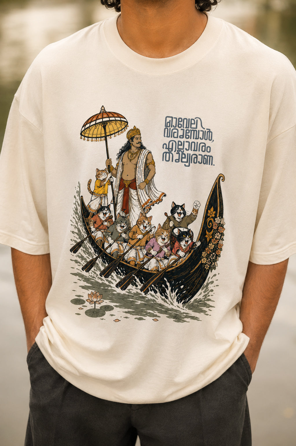 Close-up of Mild Popie's All Are Equal oversized graphic T-shirt featuring Mahabali leading a Kerala snake boat race with cats, Indian dogs, and Malayalam typography inspired by Onam.