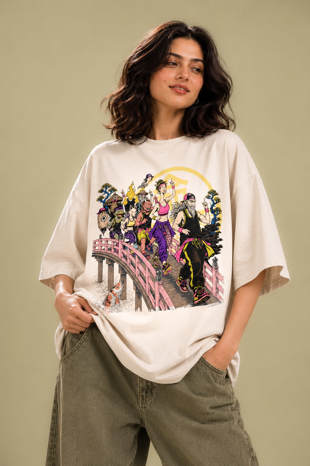 Woman wearing Mild Popie's March of Yokai premium oversized graphic T-shirt featuring colorful Japanese March of Yokai artwork, paired with olive green wide-leg pants against a beige studio background.